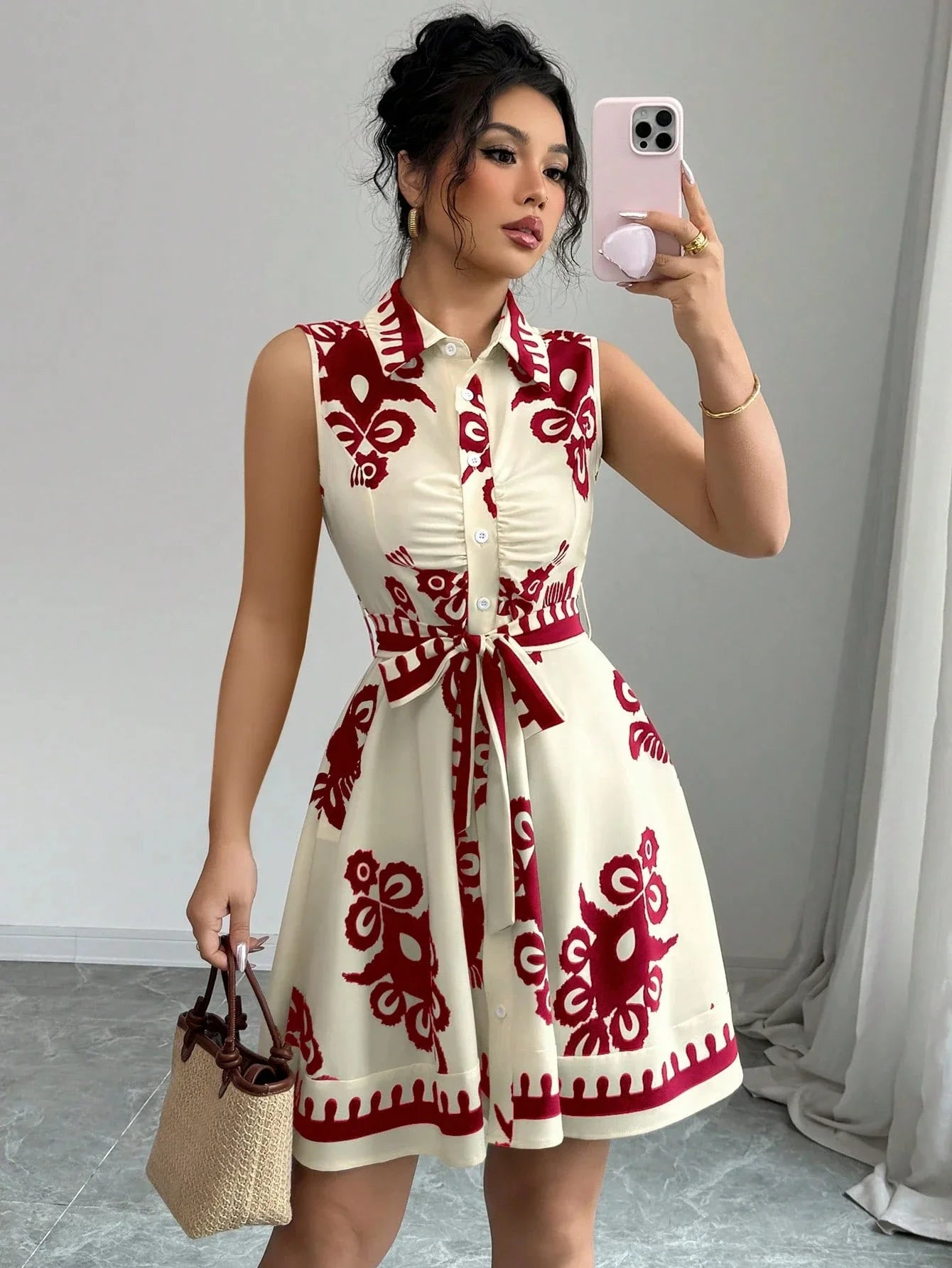 Woman taking a mirror selfie wearing a white dress with red patterns, holding a phone and a small bag.