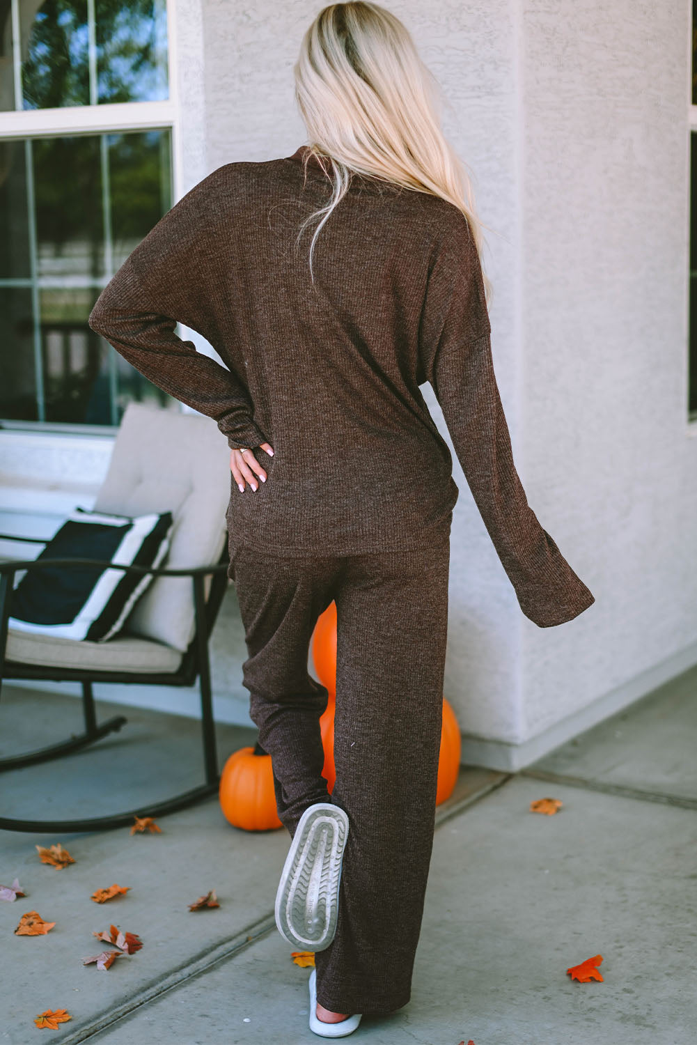 Person wearing a brown outfit standing on a patio with pumpkins and outdoor furniture.