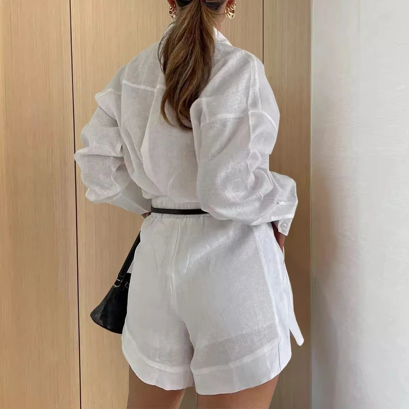 Person wearing a white outfit with a black bag against a neutral wall.
