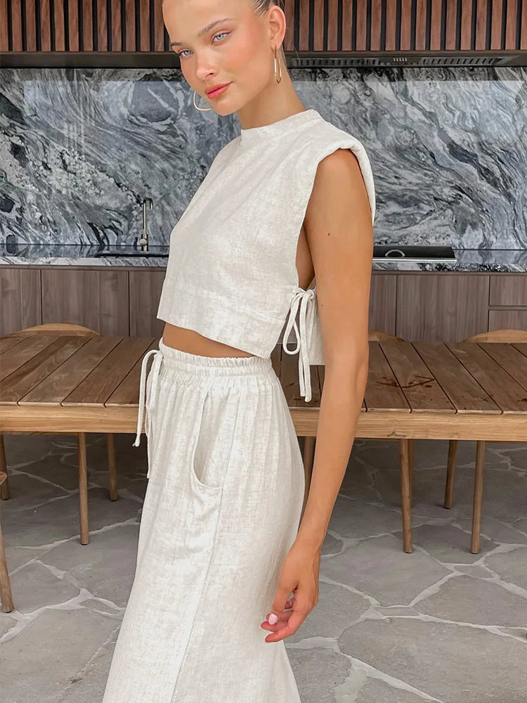 Woman in a white outfit standing in front of a marble wall.
