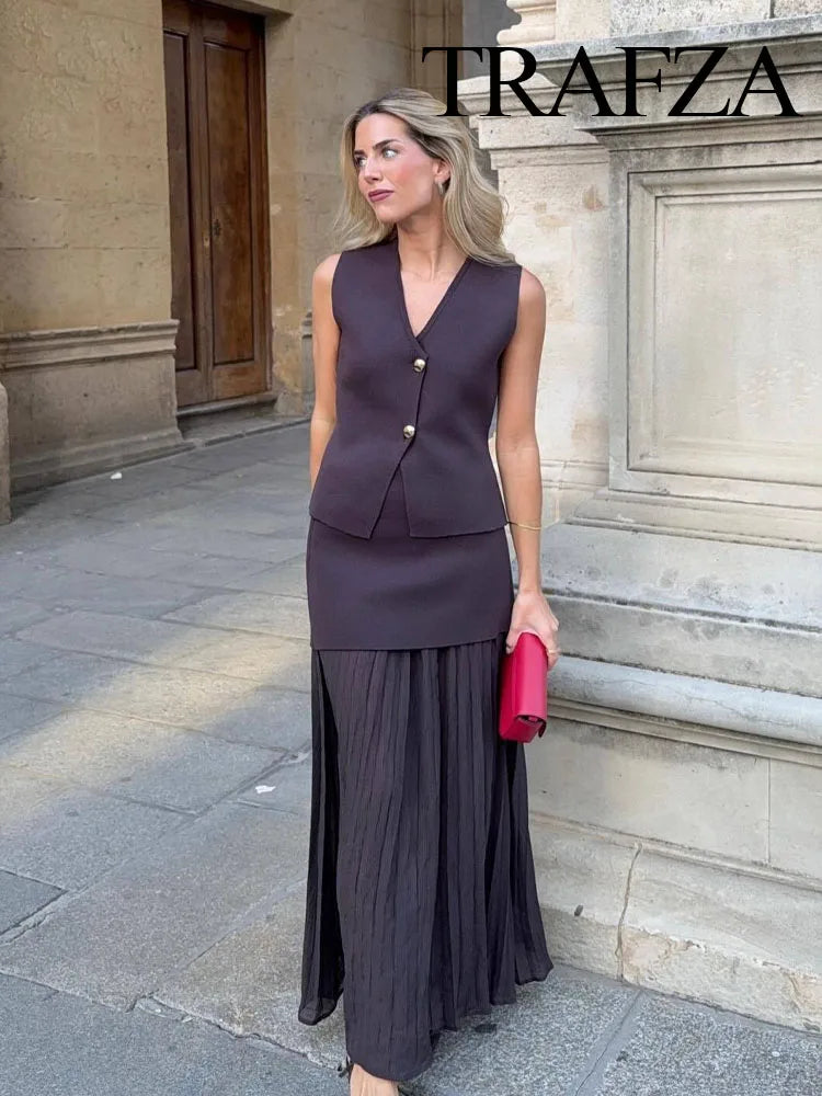Woman in a purple outfit with a red clutch standing in front of a stone building, with 'Trafza' branding.