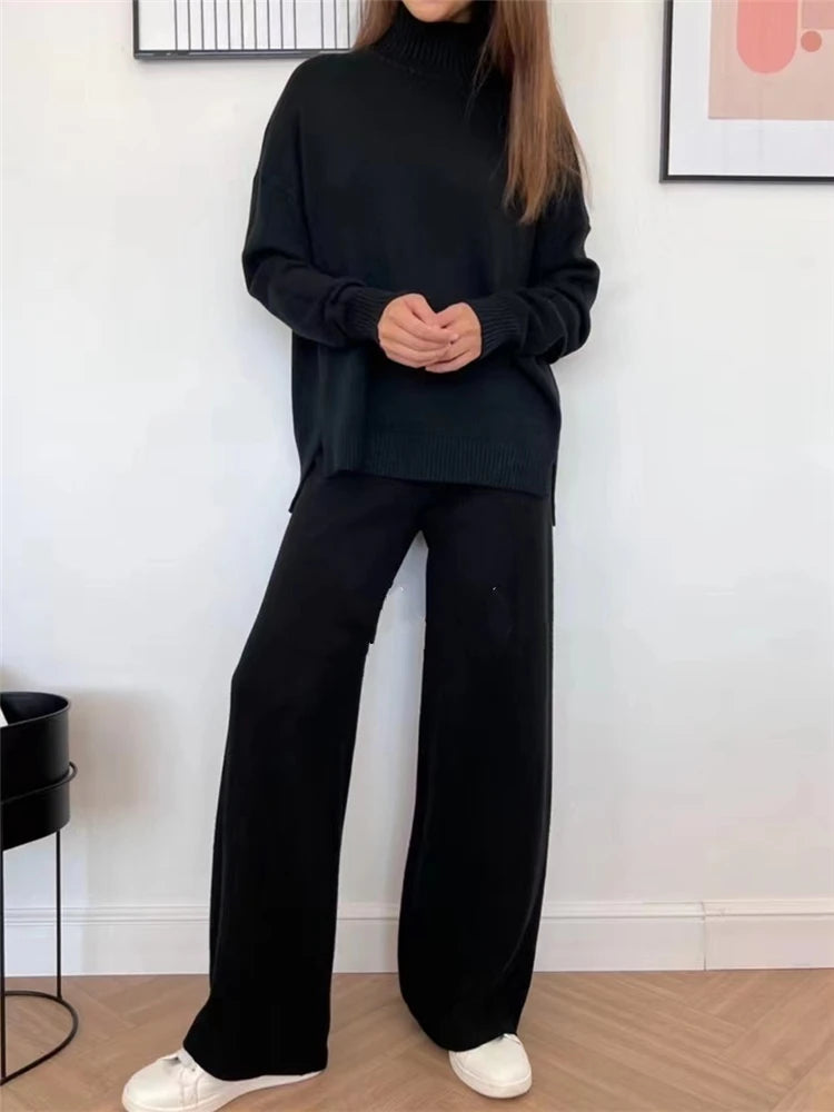 Person wearing a black outfit standing in a minimalistic room with white walls and a wooden floor.