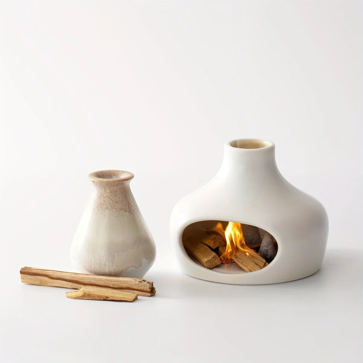 White ceramic fireplace with wooden logs and a small vase on a white background