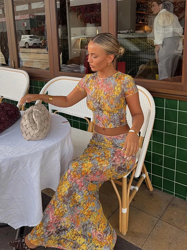 Woman in a floral dress sitting at an outdoor cafe table.