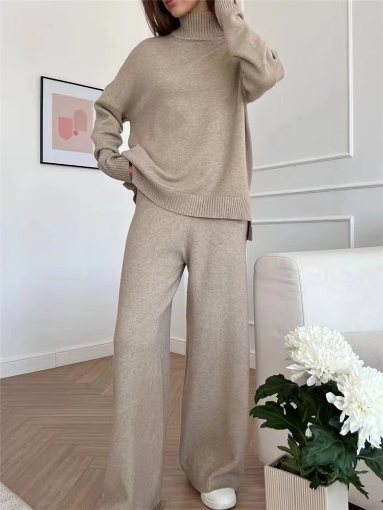 Person wearing a beige sweater and pants set in a room with a plant and framed picture.