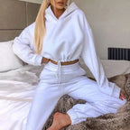Person wearing a white hoodie and pants sitting on a bed.