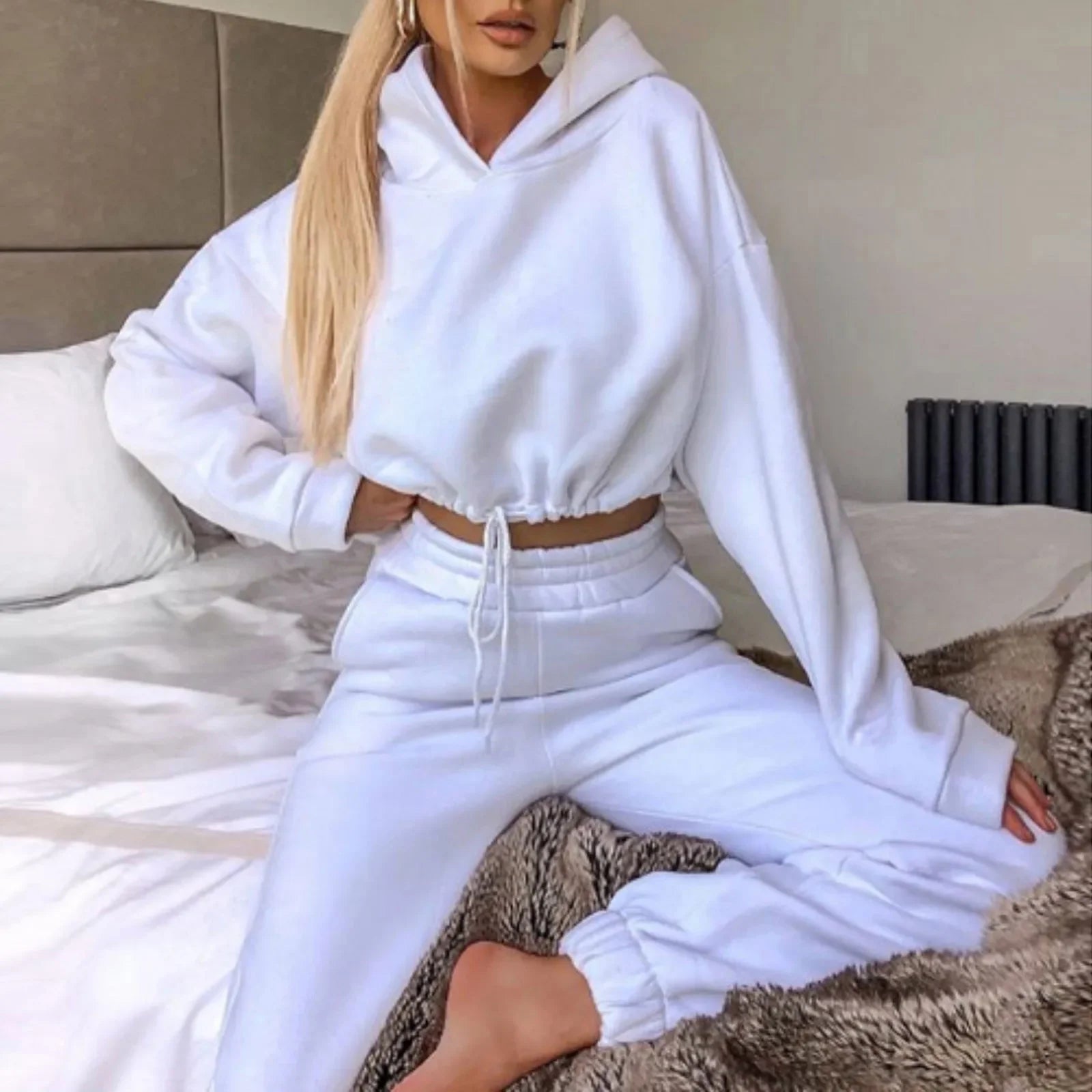 Person wearing a white hoodie and pants sitting on a bed.