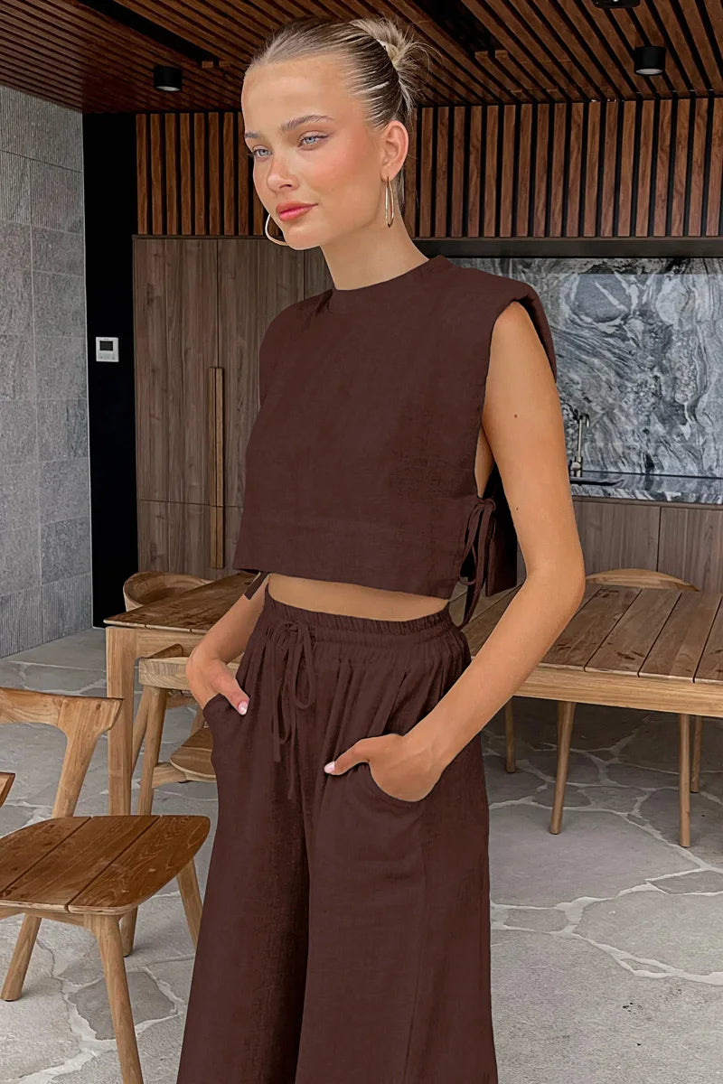 Woman in a brown outfit standing in an outdoor setting with wooden furniture.