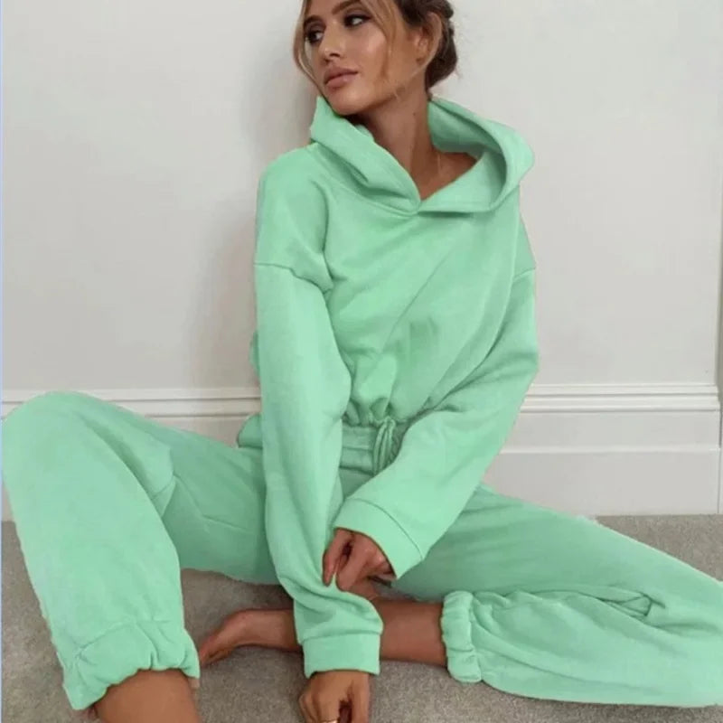 Woman wearing a mint green tracksuit sitting on the floor against a white wall.
