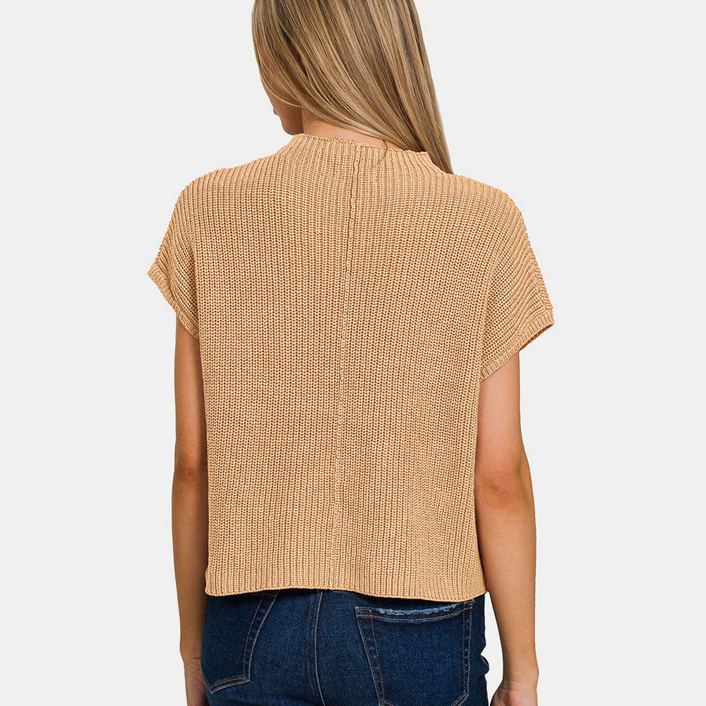 Woman wearing a beige knit top and blue jeans on a white background