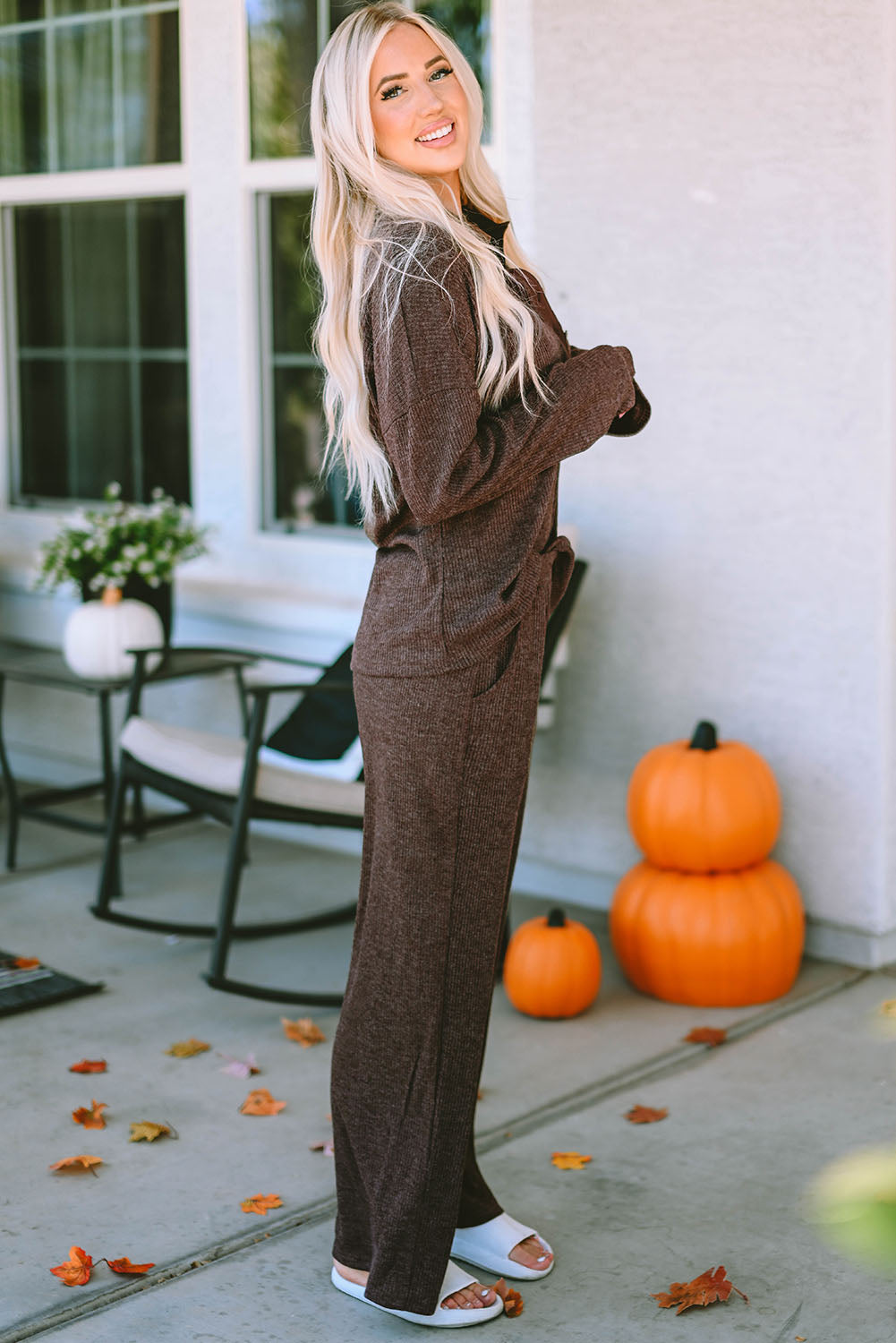 Woman in a brown outfit standing on a patio with pumpkins and leaves.