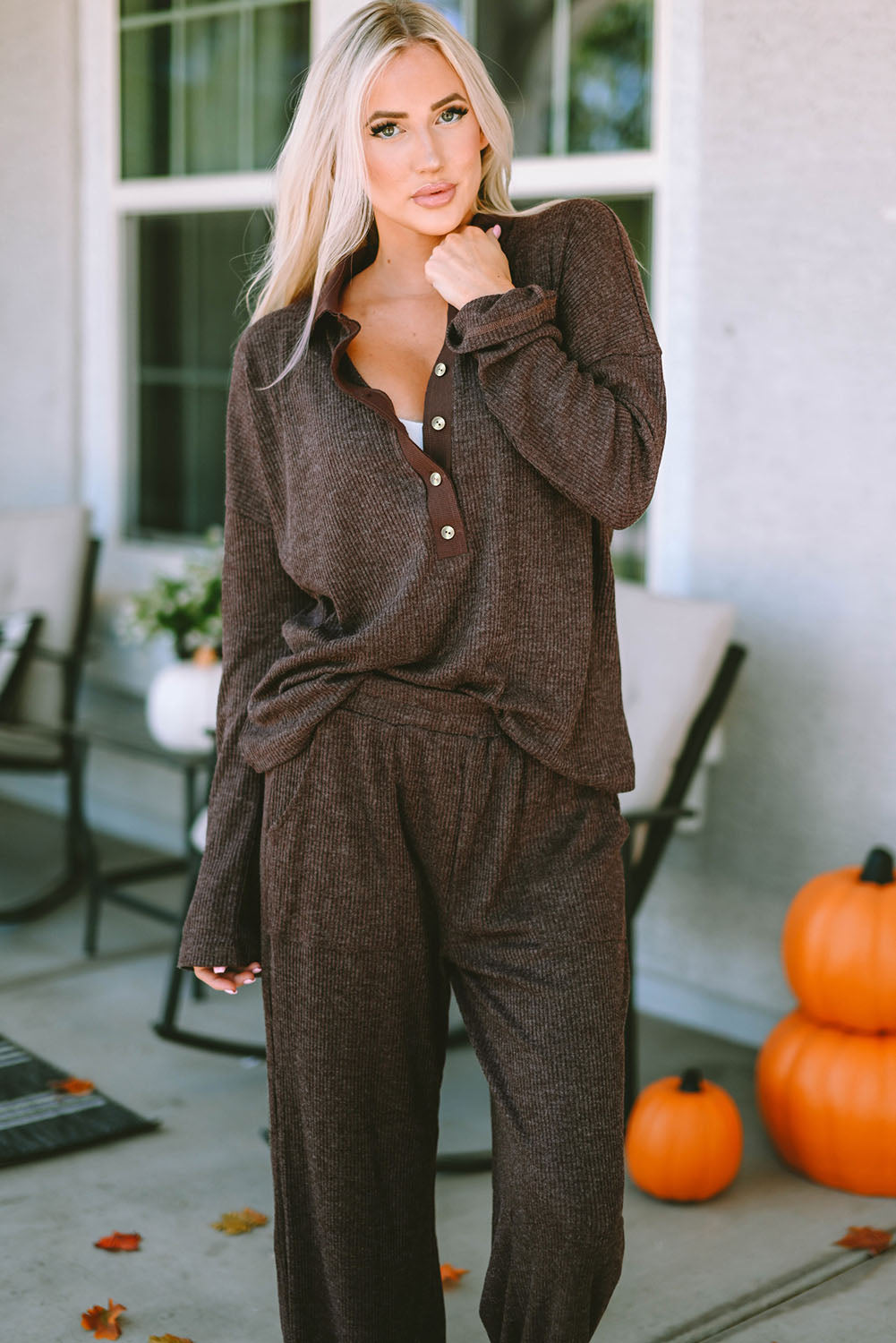 Woman in brown outfit standing on a porch with pumpkins