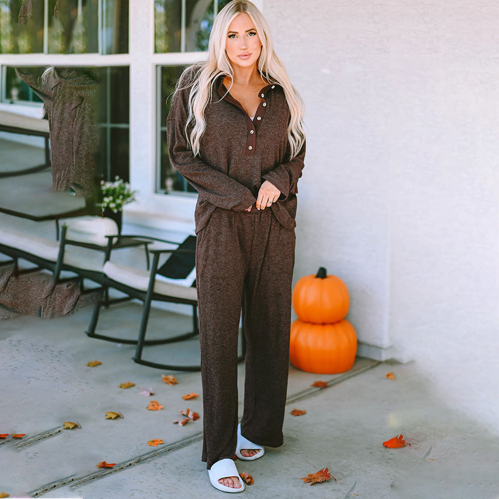Woman in a brown outfit standing on a porch with pumpkins and autumn leaves.