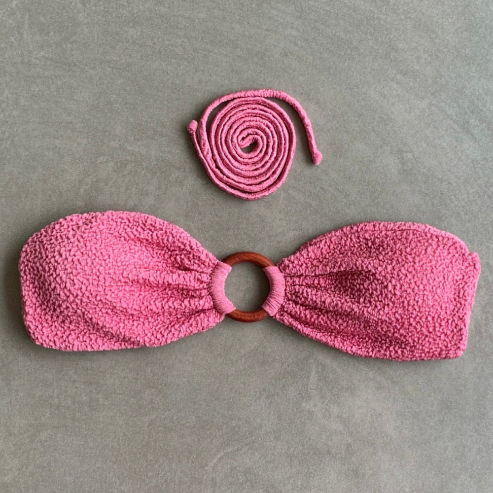 Pink textured bandeau top with wooden ring on a gray background
