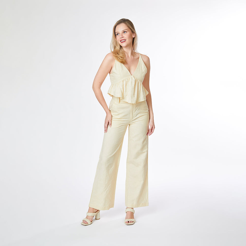 Woman wearing a light yellow ruffled top and wide-leg pants on a white background