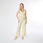 Woman wearing a light yellow ruffled top and wide-leg pants on a white background