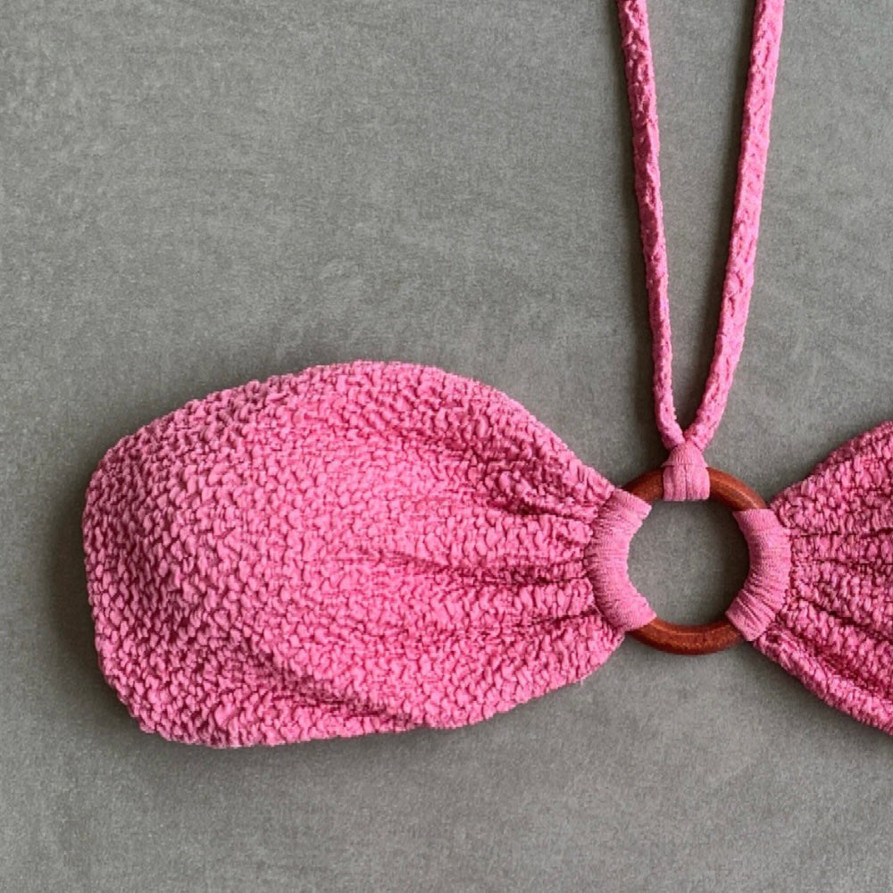 Pink textured drawstring bag with a wooden ring on a gray background