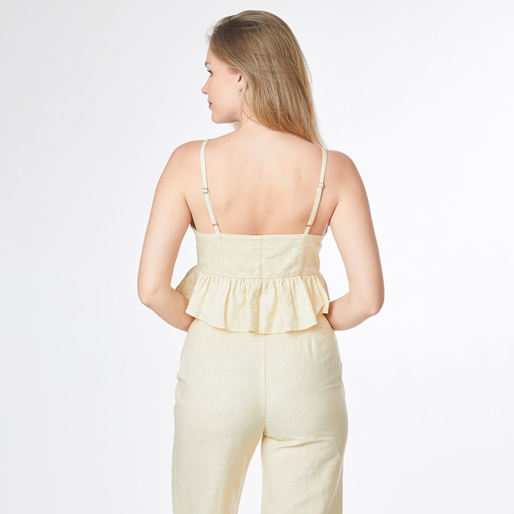 Woman wearing a light yellow jumpsuit with a ruffled top on a white background