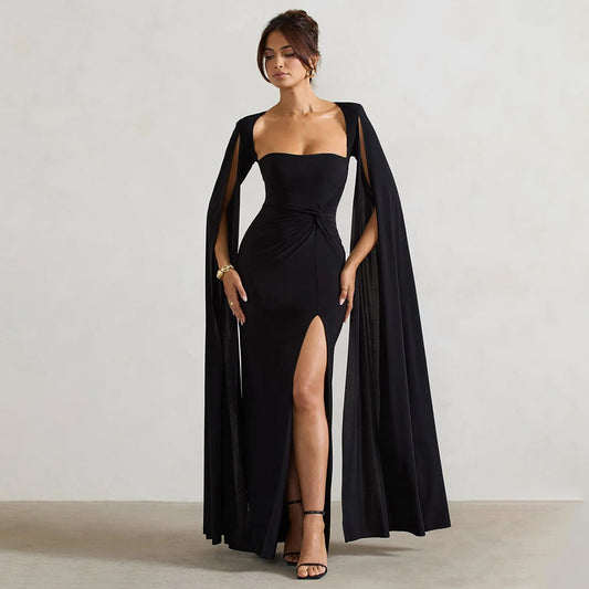 Woman wearing a black strapless gown with a long cape against a plain background