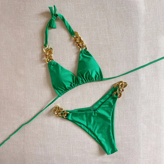 Green bikini set with gold accents on a beige fabric background