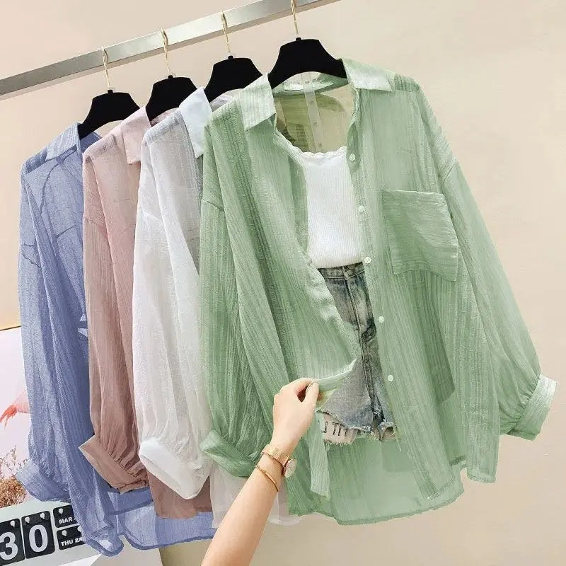 Green sheer blouse held by a hand with other sheer blouses on hangers in the background.