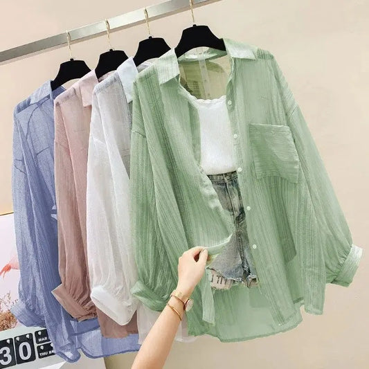 Green sheer blouse held by a hand with other sheer blouses on hangers in the background.