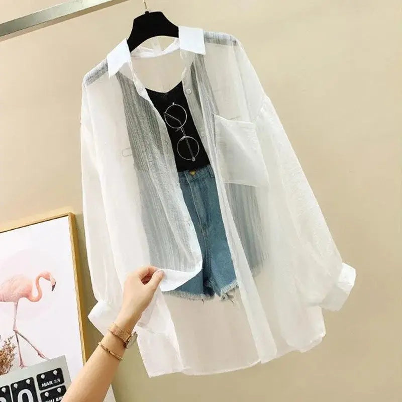 White sheer blouse over a black shirt and denim shorts on a hanger against a beige wall.