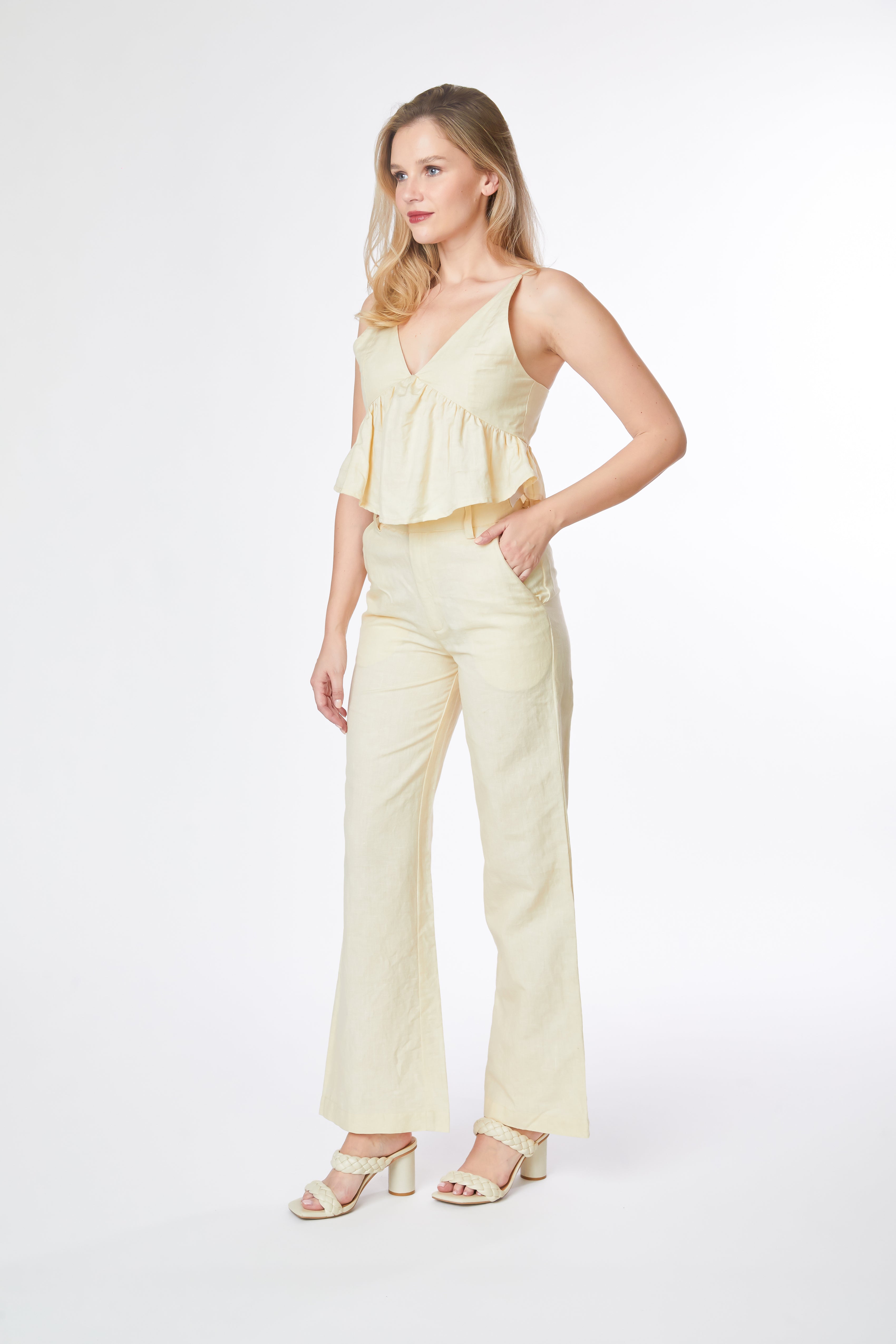 Woman wearing a light yellow sleeveless top and pants on a white background