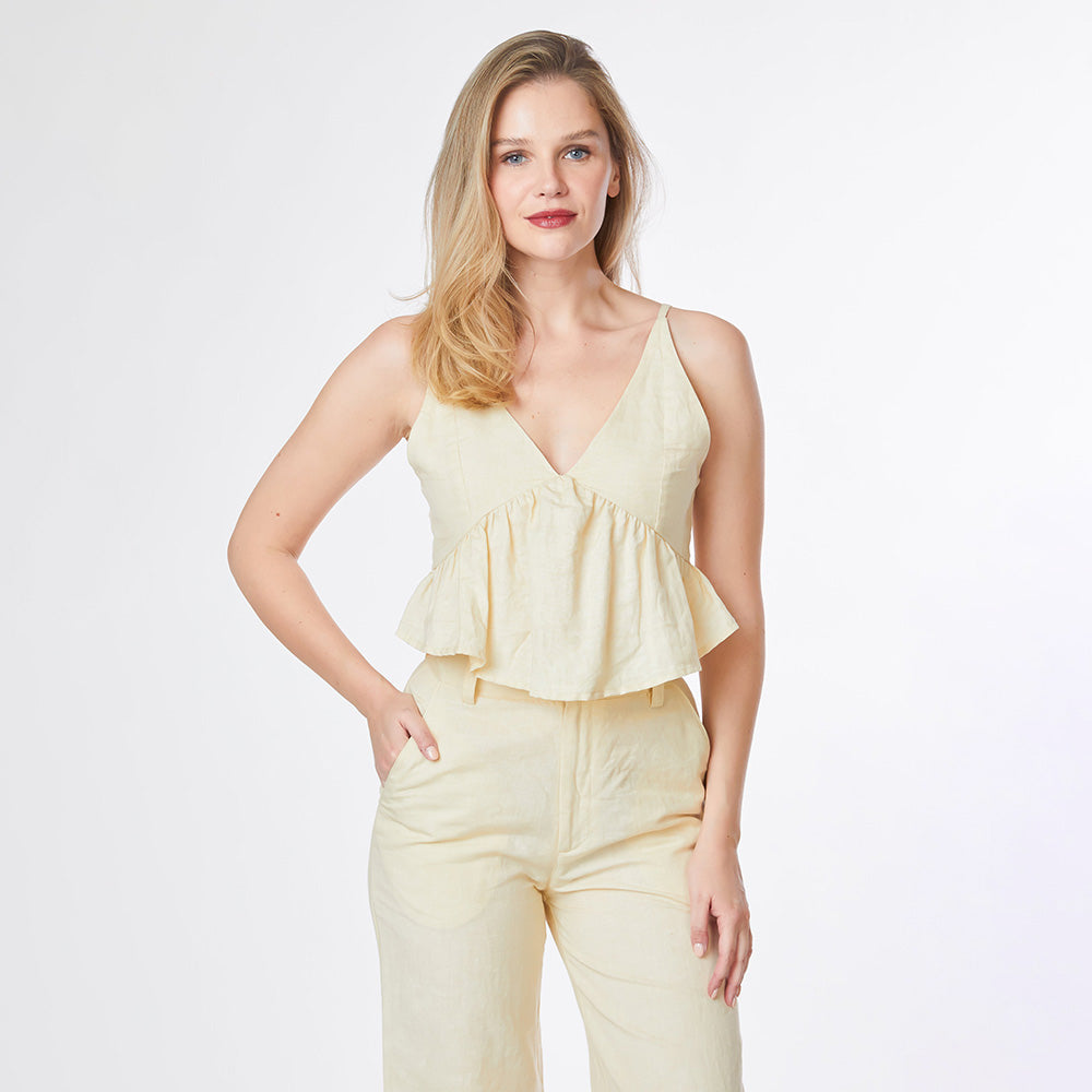 Woman wearing a light yellow sleeveless top and pants on a white background