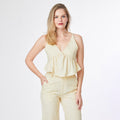 Woman wearing a light yellow sleeveless top and pants on a white background