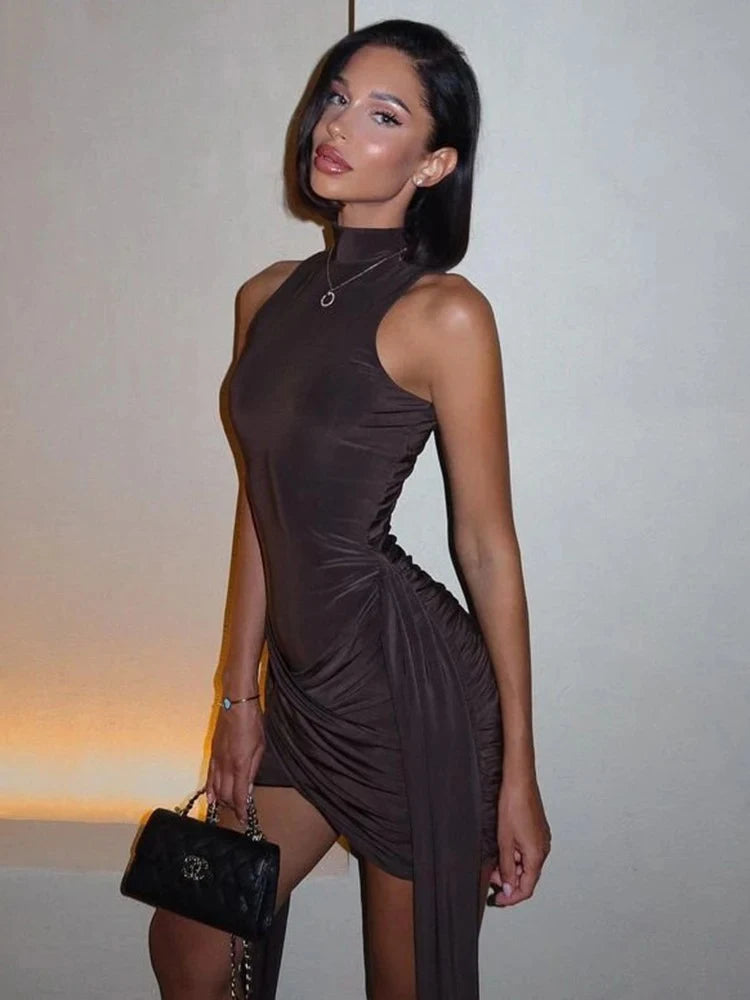Woman in a brown dress holding a black handbag against a neutral background
