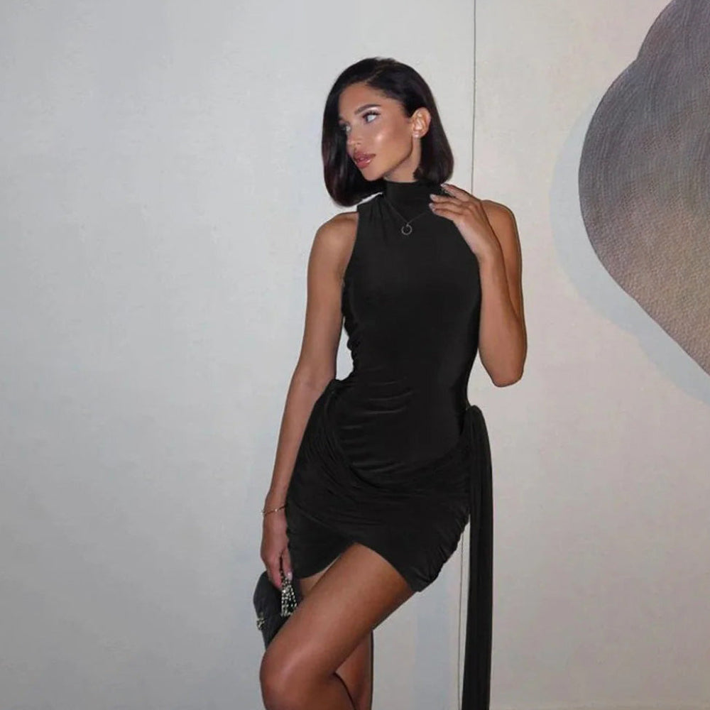 Woman in a black dress standing against a neutral wall.